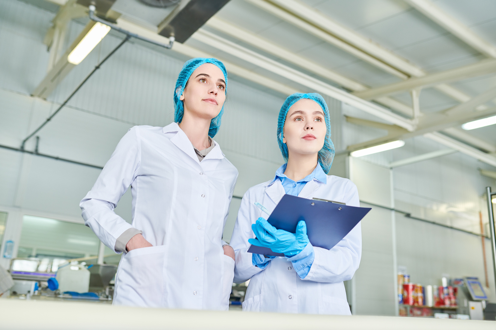 Confident purposeful female food production engineers looking at equipment while examining food manufacturing factory